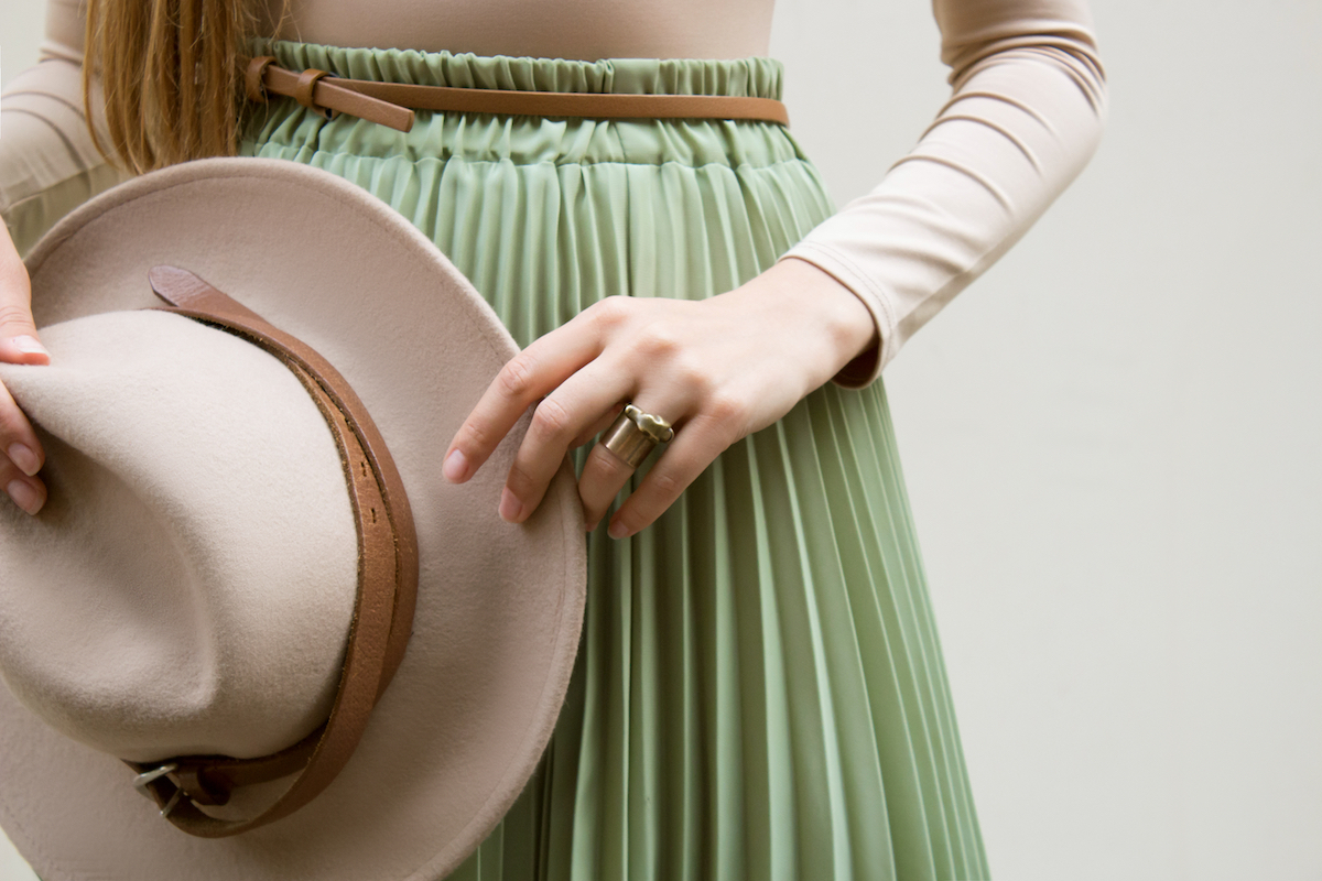 Hat, beige blouse and turqoise pleats skirt on light street backgraund.