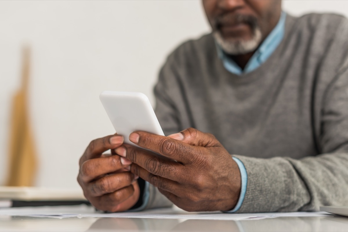 cropped view of senior man using smartphone while sitting at table