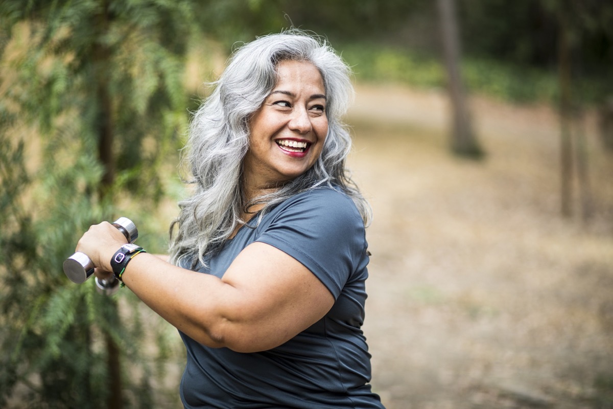 Senior Mexican Woman working out and stretching with weights in nature