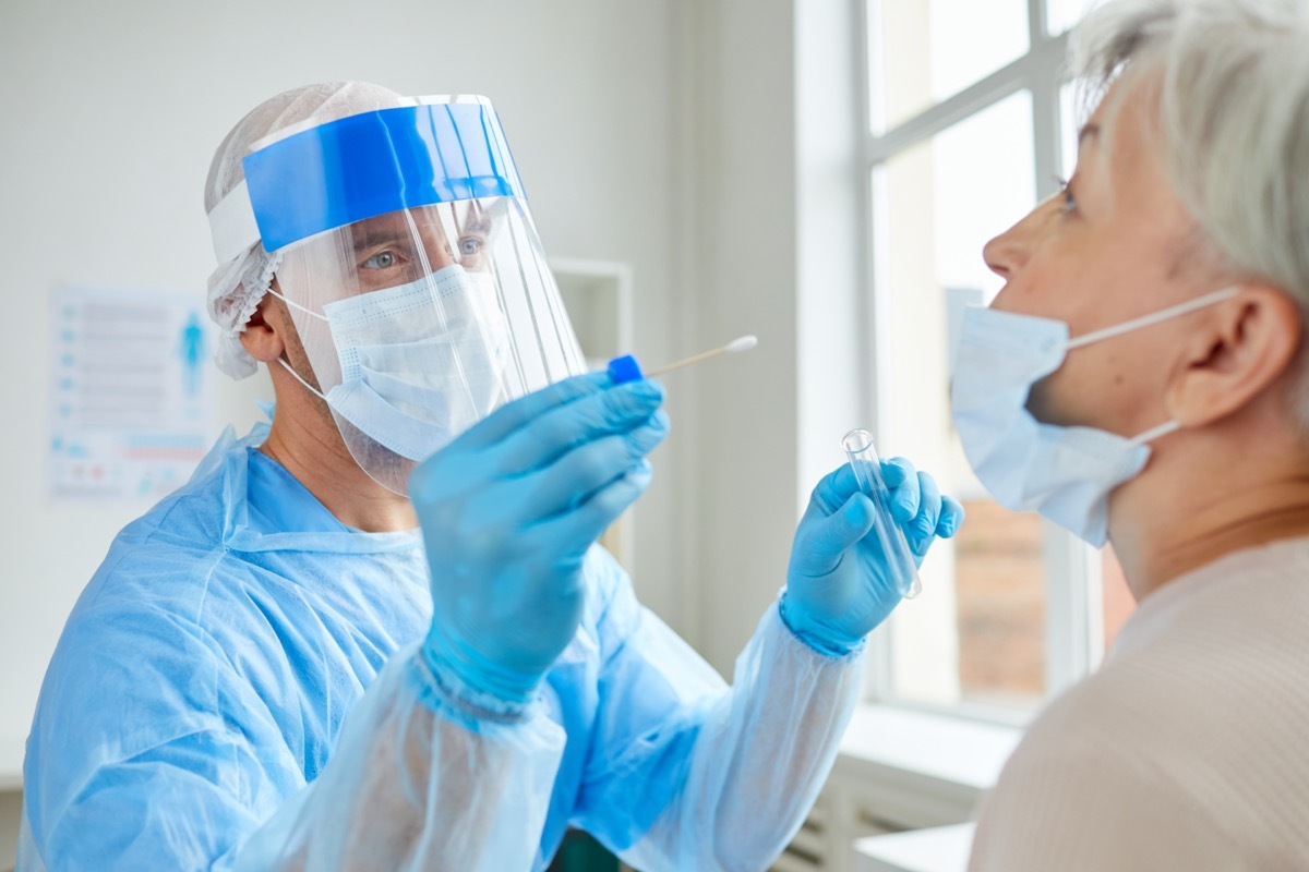 doctor in face shield and ppe giving older woman covid test