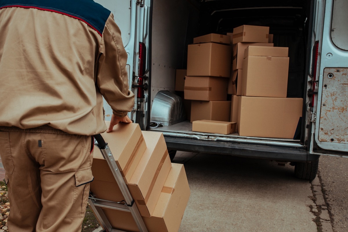 Courier packing cardboard boxes in van and preparing them for delivery