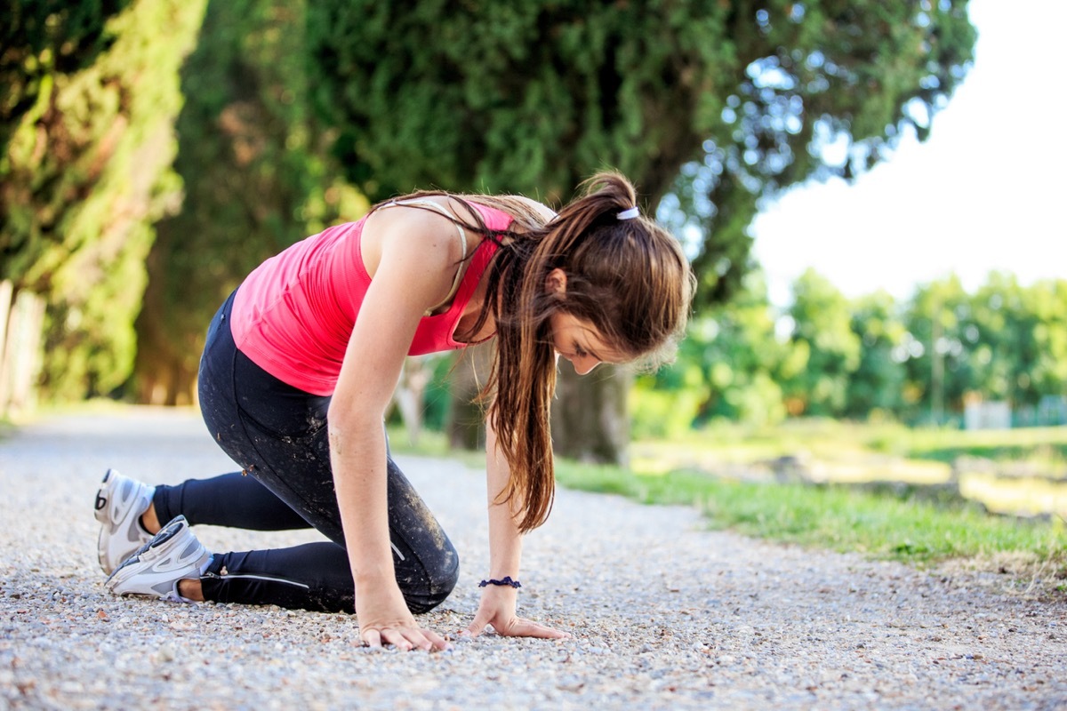 young white woman jogger getting up from the ground after falling