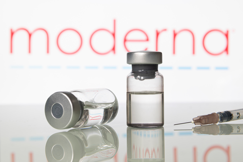 Two vials of vaccine and a syringe in front of the Moderna logo