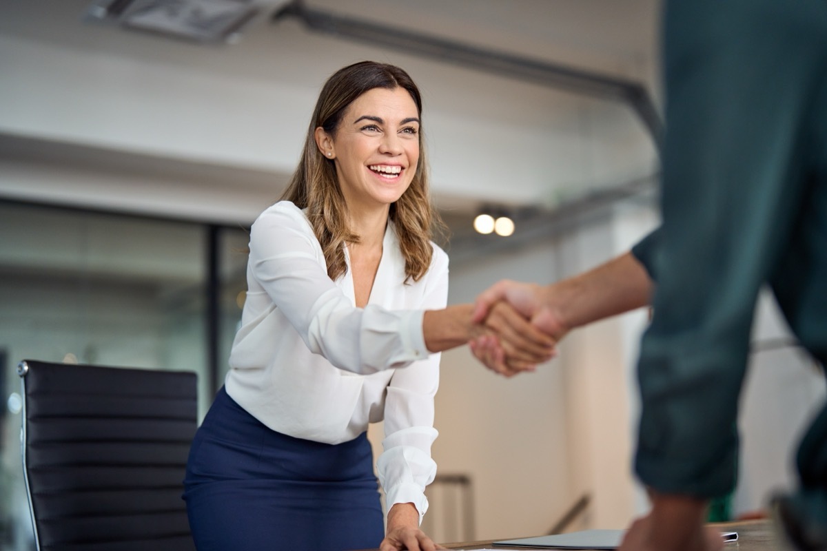 Smiling female executive shaking hands at work standing at her desk