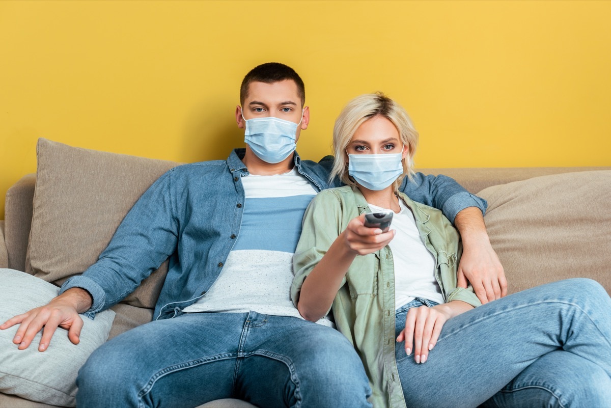 young couple watching TV with masks