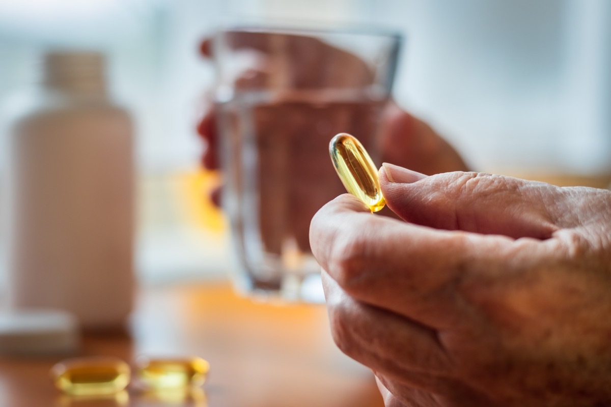 Senior woman holding omega-3 fish oil nutritional supplement and glass of water in her hands.