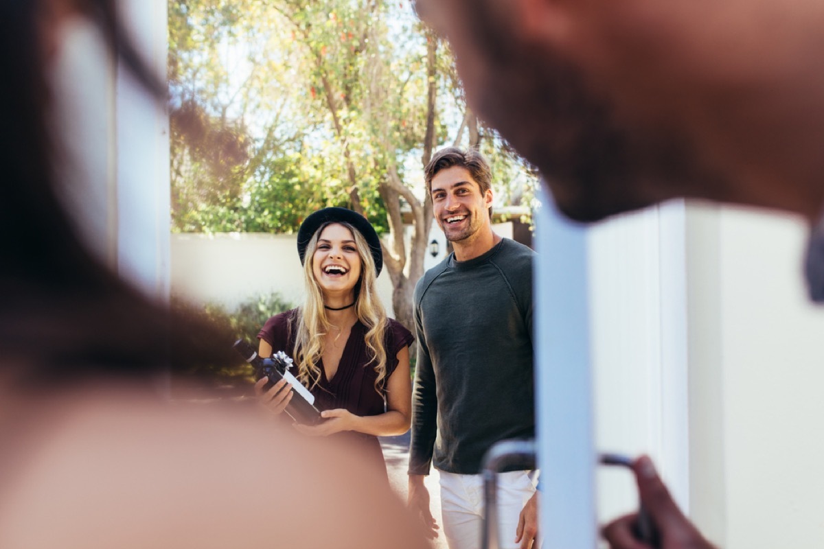 couple arriving at party with bottle of wine, housewarming gifts