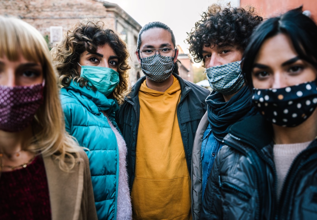 crowd of citizens in city street covered by face mask looking at camera - New normal lifestyle concept with people worried about pandemic virus - Focus on guy in the middle