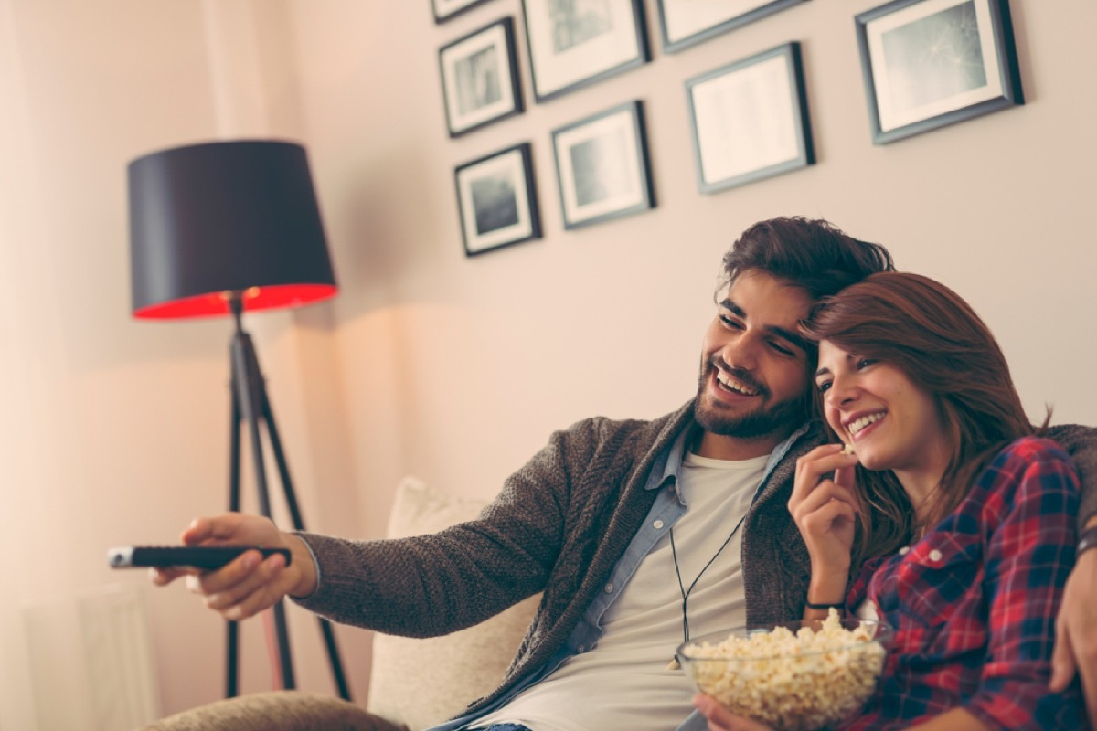 young man and woman watching tv and eating popcorn on the couch