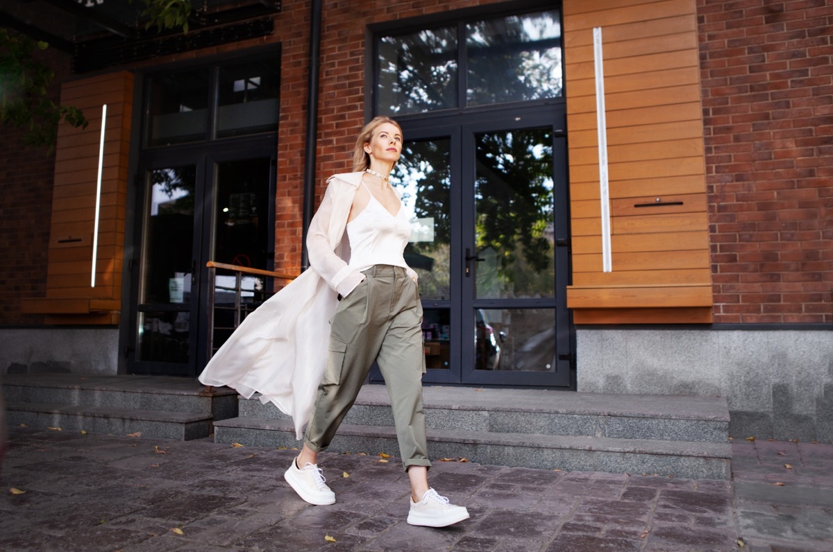 Beautiful Woman Wearing Fashionable Spring, Fall Clothes (beige trench coat, oversize khaki cargo pants, accessorie) Outdoors. Female stylish Model walking city Street. Autumn trend, fashion outfit