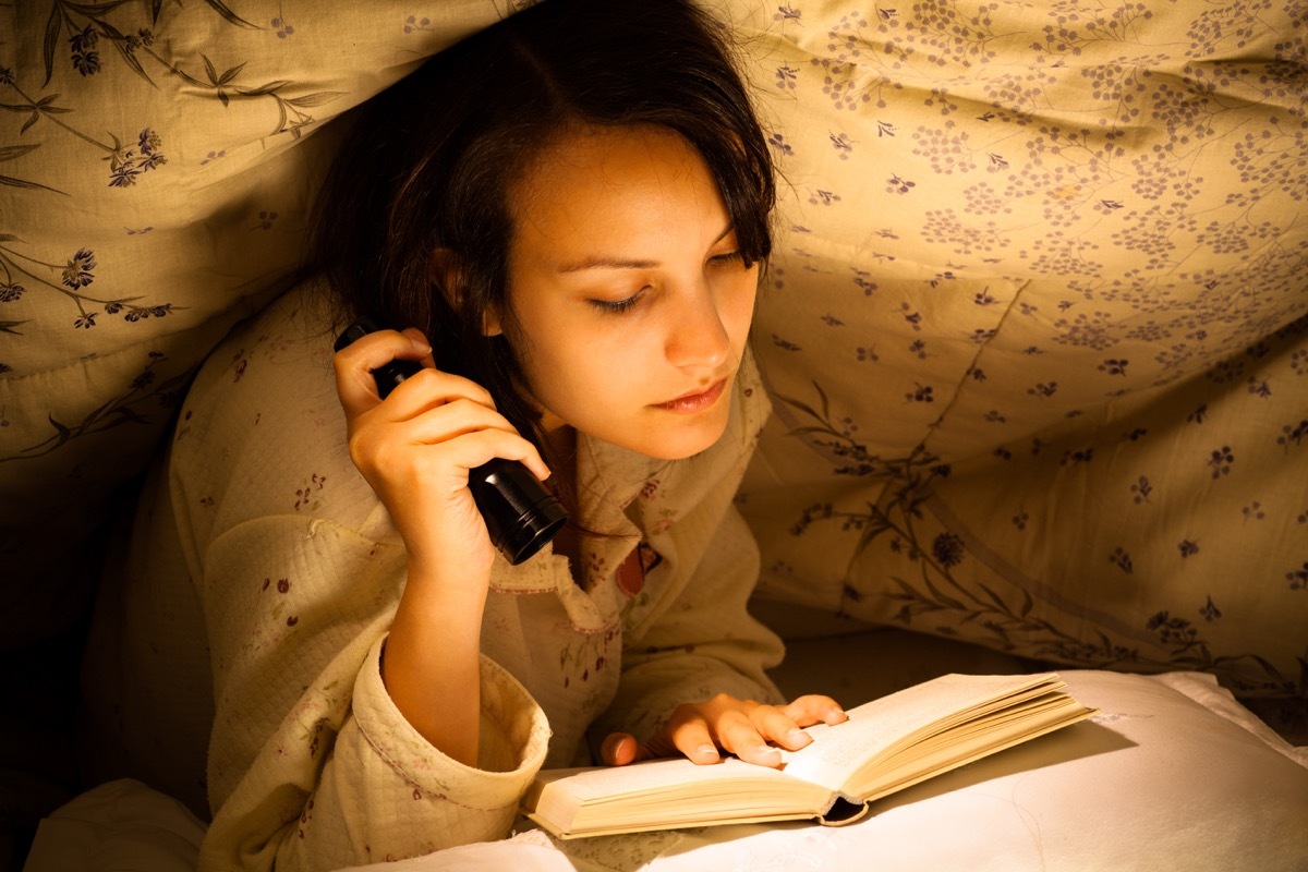 Woman reading by flashlight