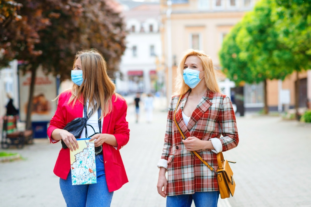 two white women with face masks walking through a city