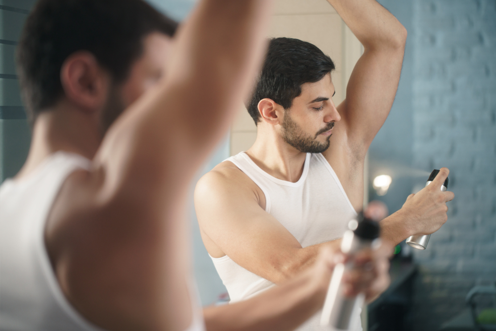 A young man applying spray deodorant