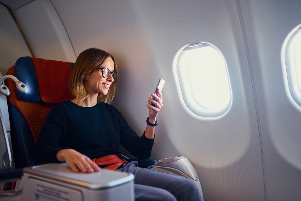 woman sitting in bulkhead airplane seat, smiling at phone