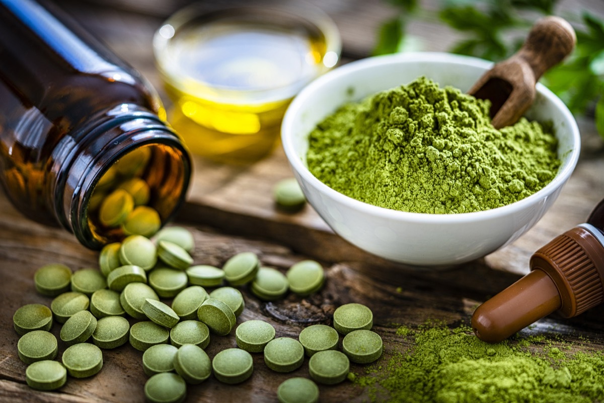 Nutritional supplement: Moringa powder in a white bowl and Moringa capsules spilling out a bottle shot on rustic wooden table. High resolution 42Mp studio digital capture taken with Sony A7rII and Sony FE 90mm f2.8 macro G OSS lens