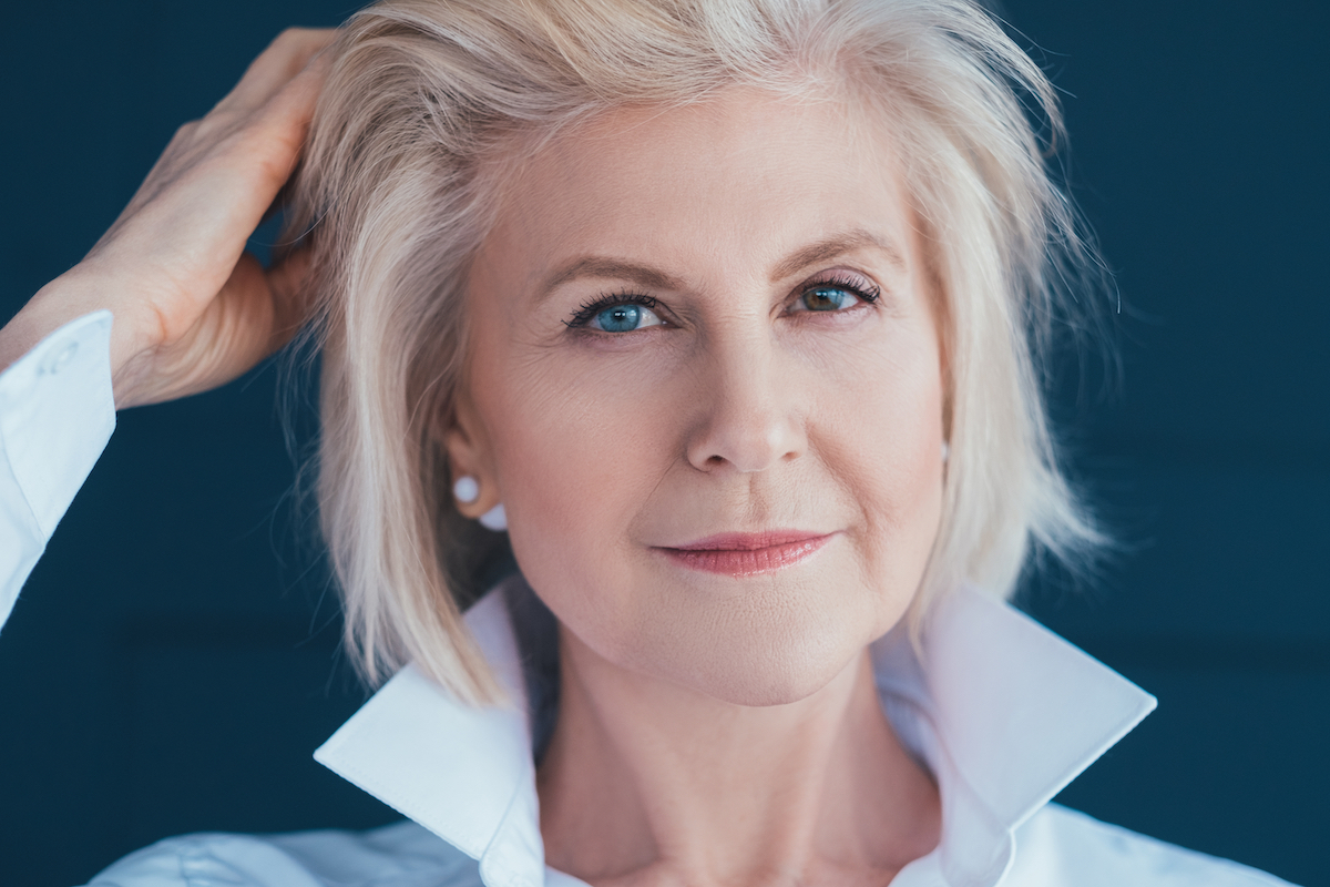 Close up portrait of an attractive older woman running her hand through her short, white/blonde hair.