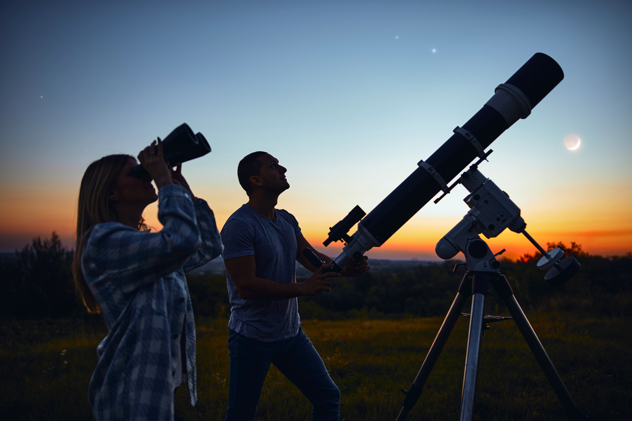 A couple using binoculars and a telescope to stargaze