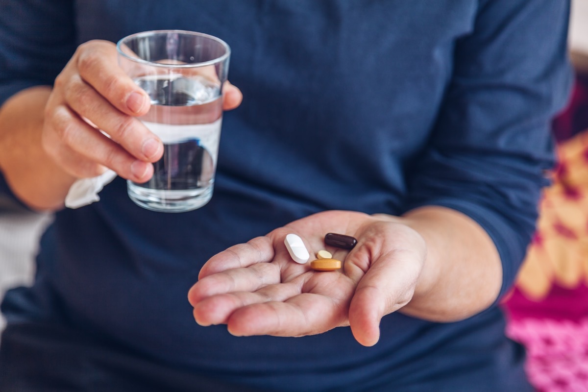 Senior woman holding medical pills and a glass of water on the bed