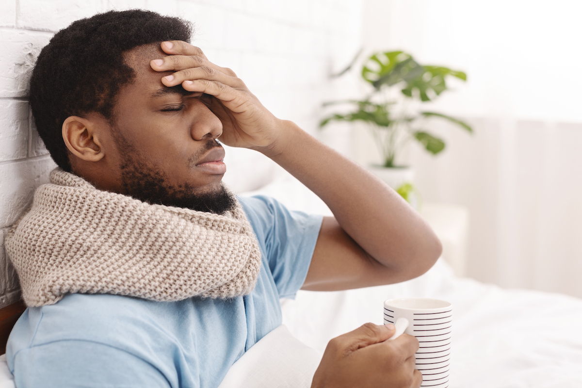 Sick man having fever, drinking hot tea and touching forehead