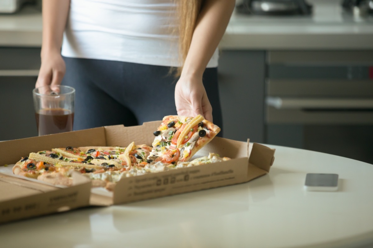 Female hands taking a slice of pizza from the box on the kitchen table, close up