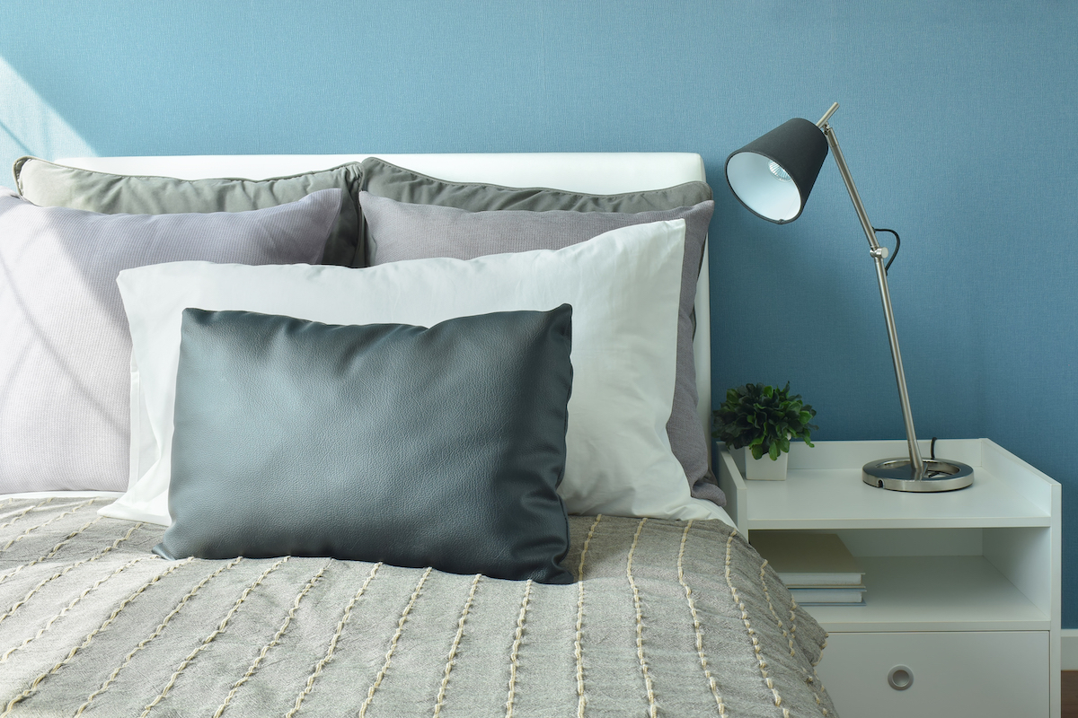 Gray, dark gray and white color pillows on bed with modern style table lamp and blue walls