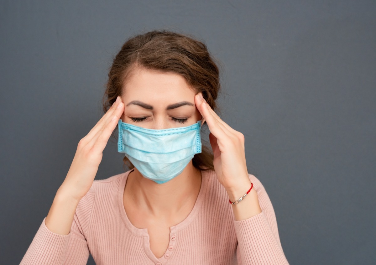 young brunette girl in medical mask holds her head