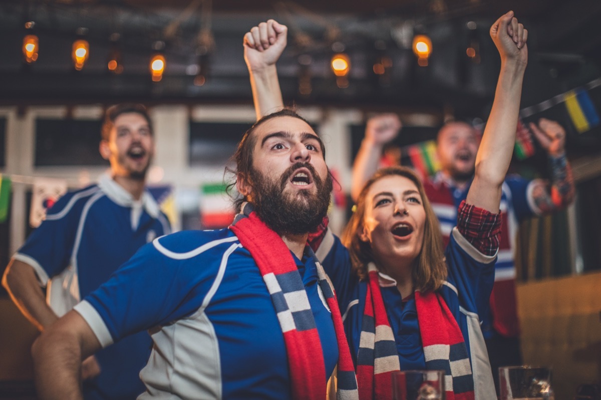 Group of close friends watching a game at the bar and cheering for their team.