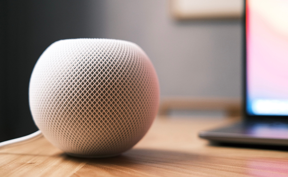 A white Apple HomePod Mini sitting on a desk next to a laptop.