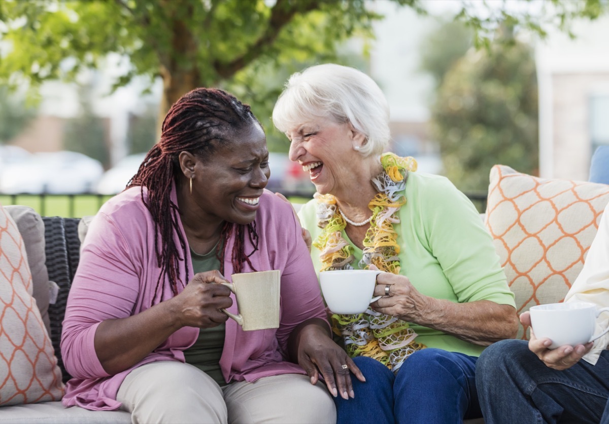 two older female friends laughing over a cup of coffee