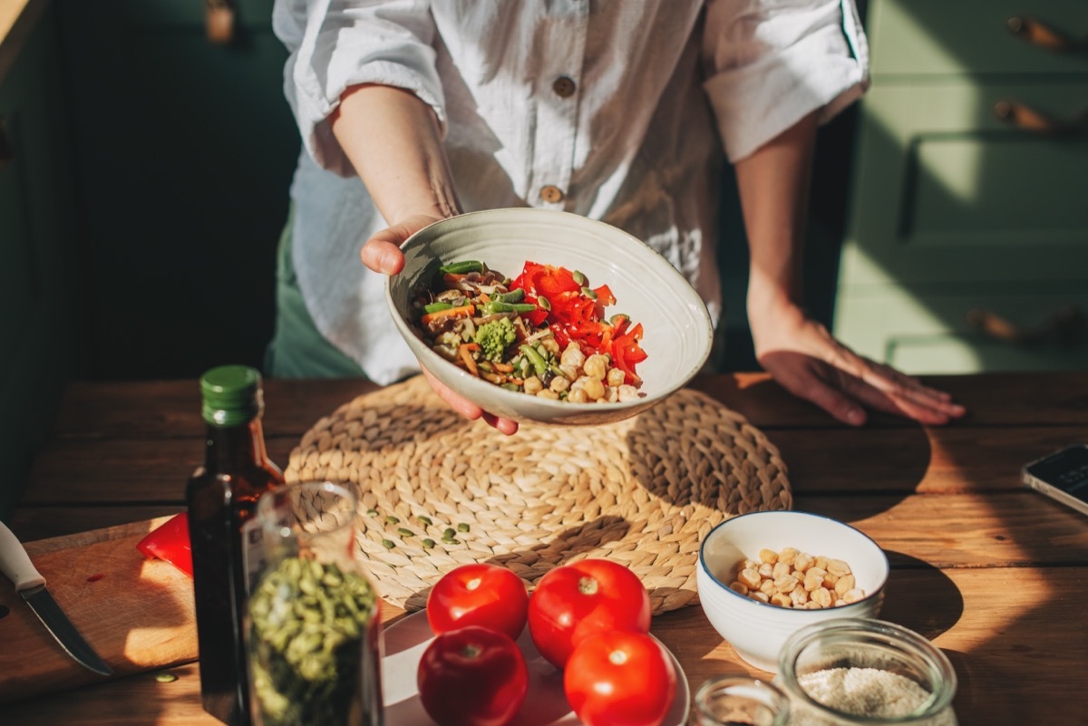 Cropped image of a person holding out a bowl of healthy food while standing over a wooden counter filled with healthy ingredients