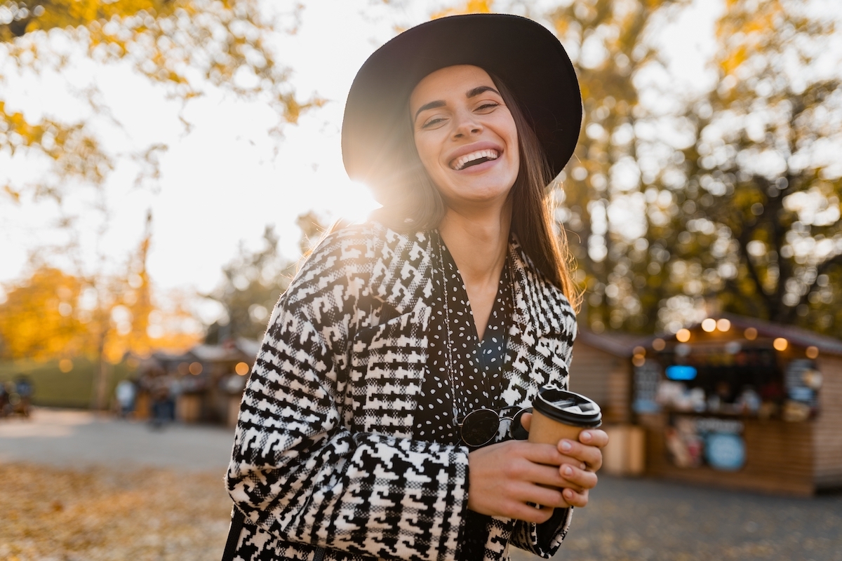 attractive young woman walking in autumn street wearing checkered coat, black hat