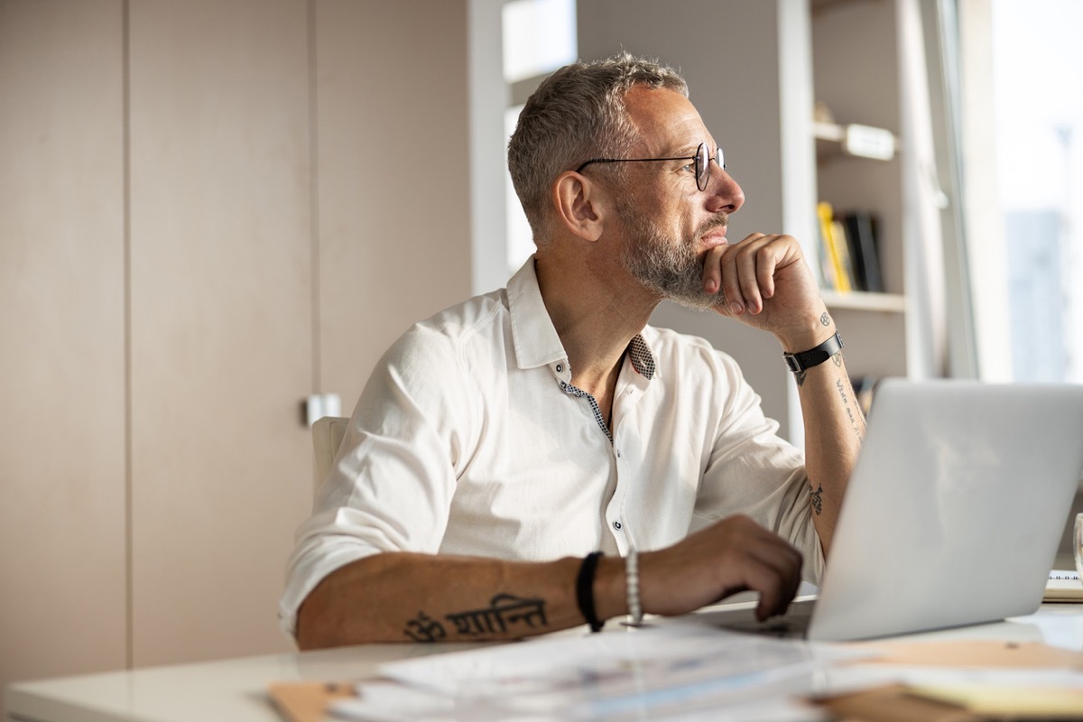 Philosophical person propping up his chin with a hand and getting distracted from working process with something outside