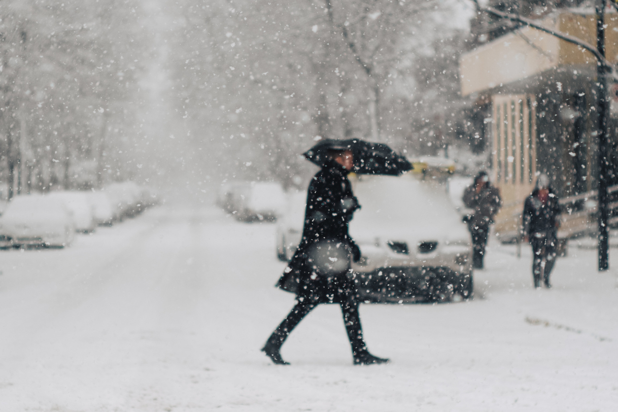 A person crossing the street during a snowstorm while using an umbrella