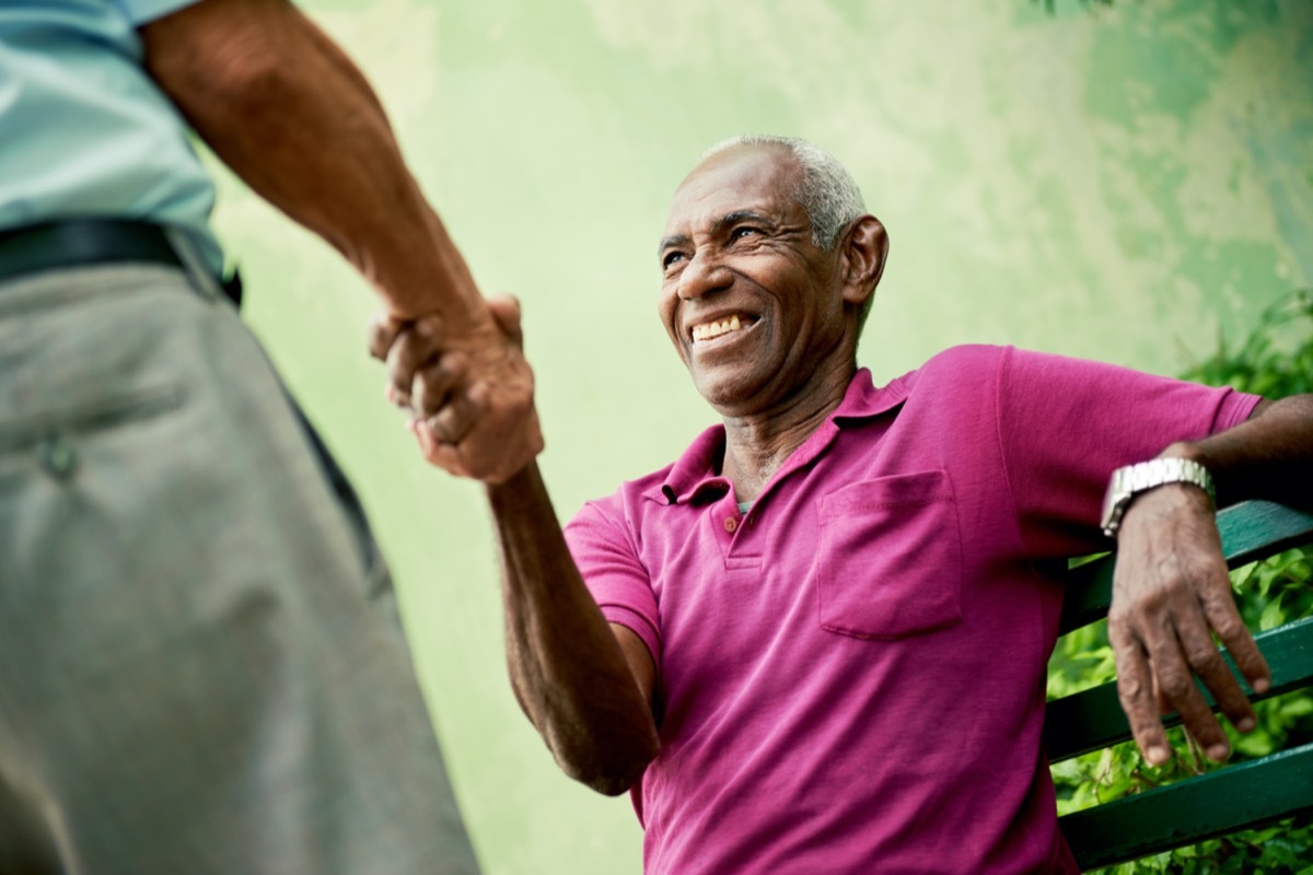 retired elderly people and free time, happy senior african american and caucasian male friends greeting and sitting on bench in park